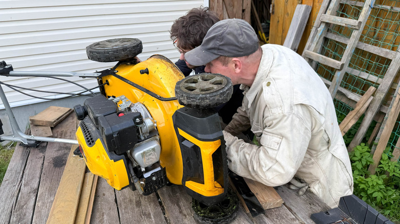 Two men examining the underside of a lawn mower
