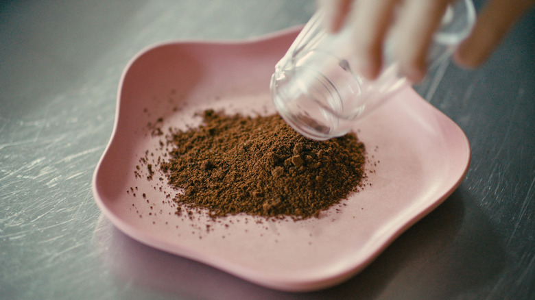 A jar pouring coffee grounds onto a pink plate