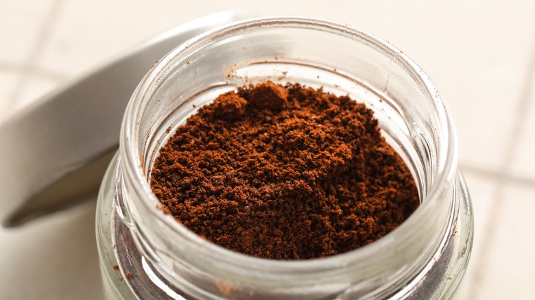 A jar of ground coffee on a tile surface