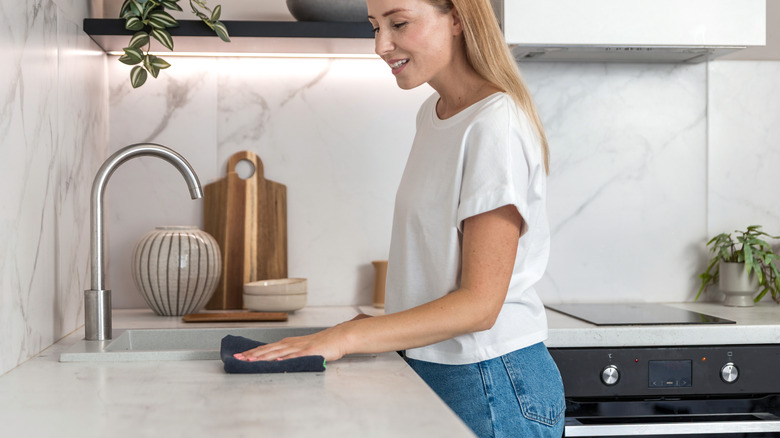 A person wiping down a white marble kitchen countertop