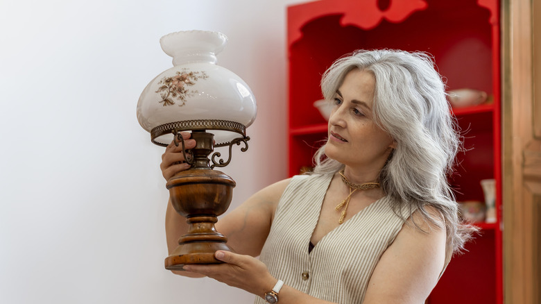 Gray-haired woman examining an old kerosene lamp inside a vintage shop.