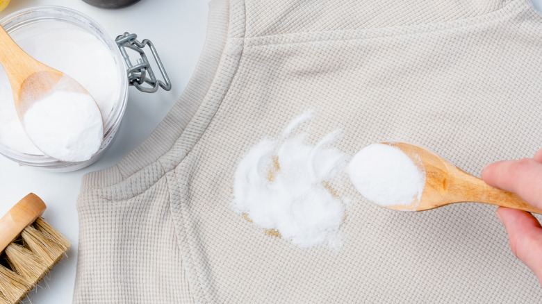 Hand sprinkling spoonful of baking soda onto a garment