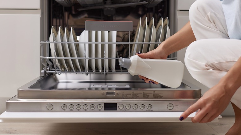 A person pouring liquid detergent into a dishwasher