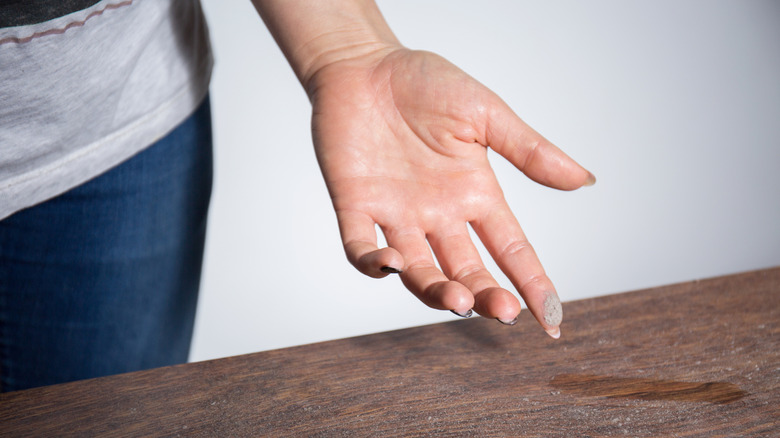 Person wiping a finger through dust on a table