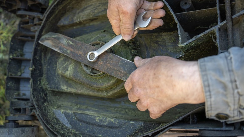 Person loosening lawn mower blade while holding the blade steady with a hand.