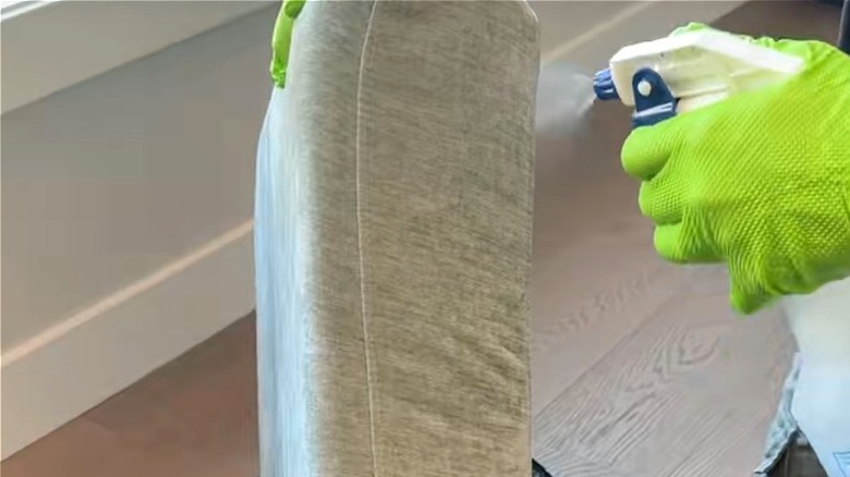 Man deodorizing a couch cushion with vinegar spray