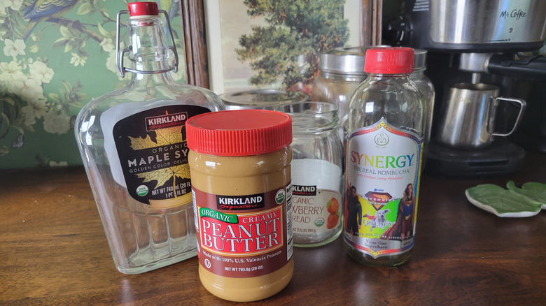 A jar of peanut butter and some bottles and jars with labels to be removed