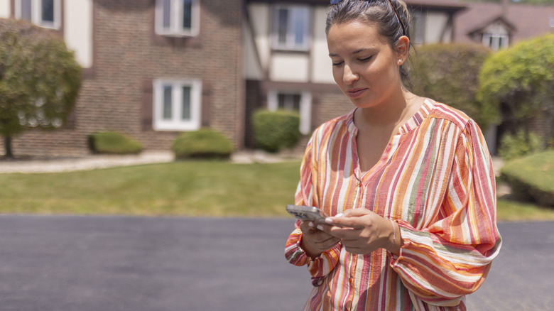 A woman scrolls on her phone by her driveway