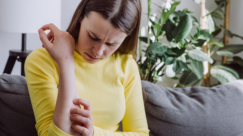 A woman in a yellow top holds her arm after being bitten by an insect