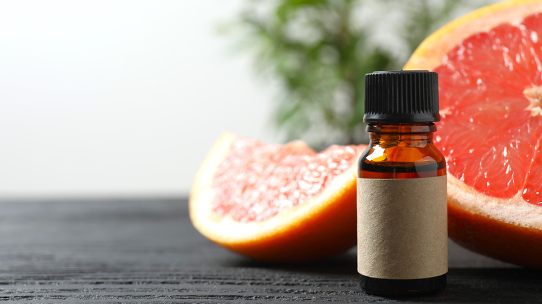 Bottle of grapefruit essential oil on table in front of a cut grapefruit