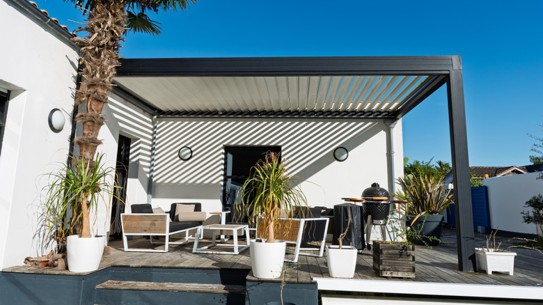 Furniture, grill, and potted plants under a louvered pergola