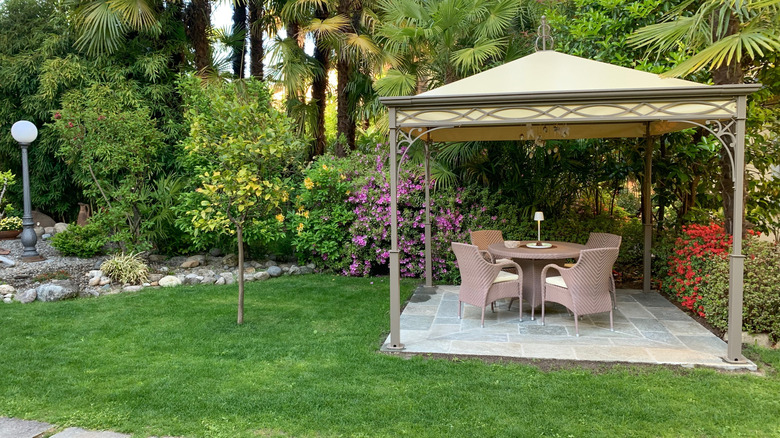 A gazebo in a garden with a small table and four chairs beneath it