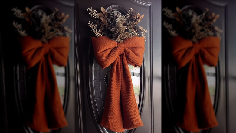 Cute front door decor idea with oversized orange bow with dried grasses and fall foliage on ornate glass front door
