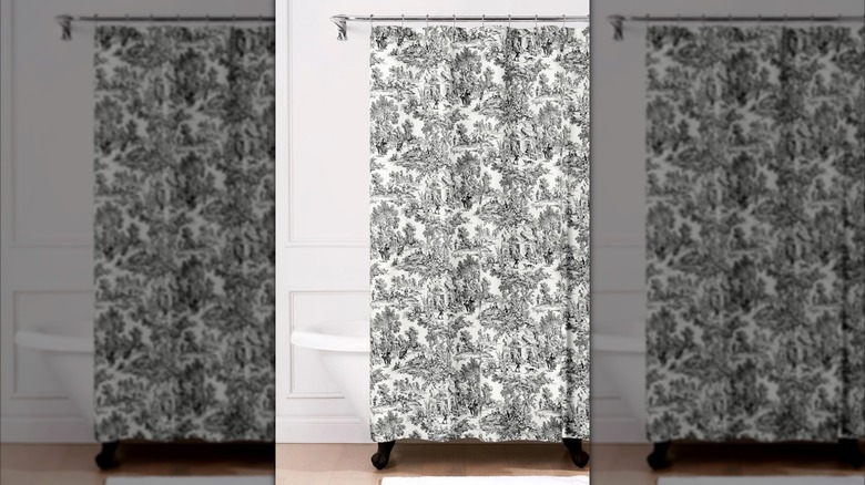 A black and white toile shower curtain on a silver rod around a bath