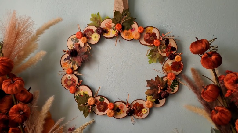 Pressed flowers, mini pumpkins, and fall-esque leaves on a wood slice wreath