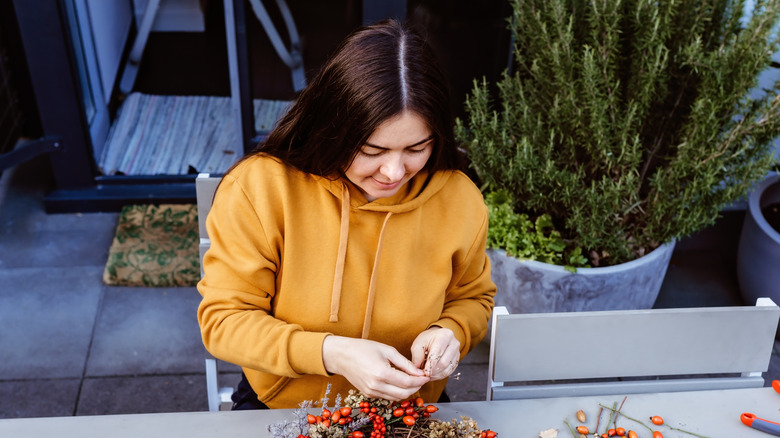 A woman in a yellow sweater arranges fall foliage on an outdoor table