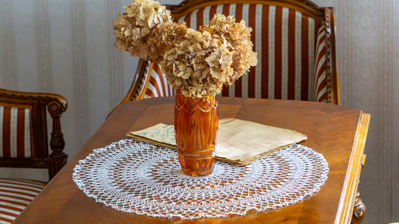 Orange vase of flowers on doily-dressed table