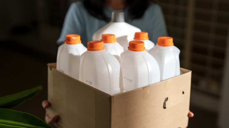 Box of empty plastic bottles held by a person in the background