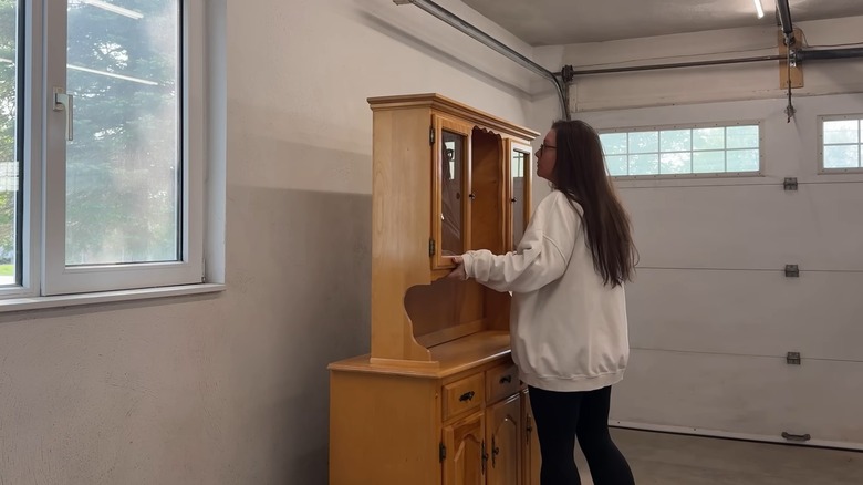 DIYer in white cardigan picking up the top of an old hutch for an upcycling project