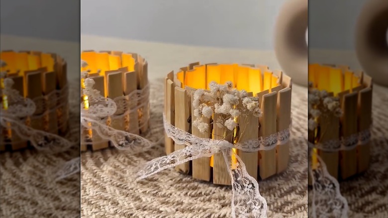 Tealight candle lit up inside clothespin candleholder with lace ribbon and white flowers on rustic mat
