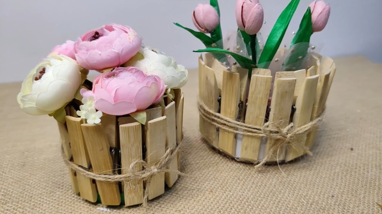 Clothespins and jar lid upcycled to hold artificial pink and white flowers on beige fabric