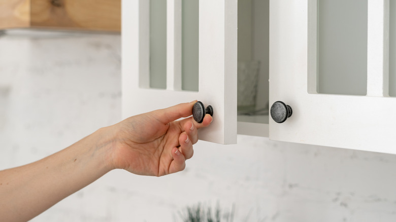 Hand on kitchen cabinet knobs, opening the door