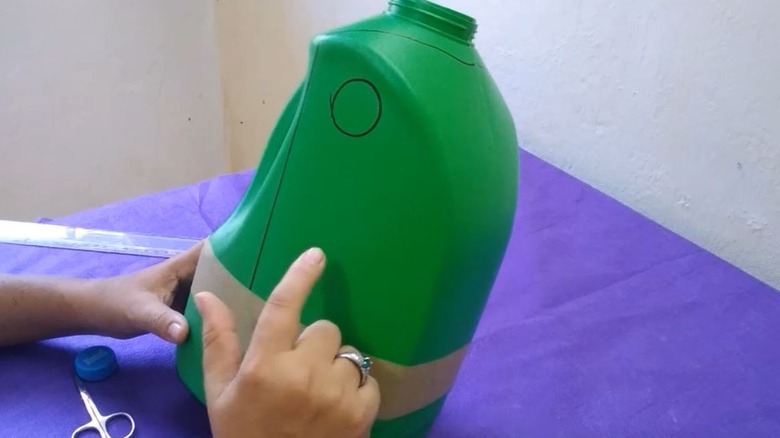 Woman turning old detergent bottle into a toilet paper storage solution