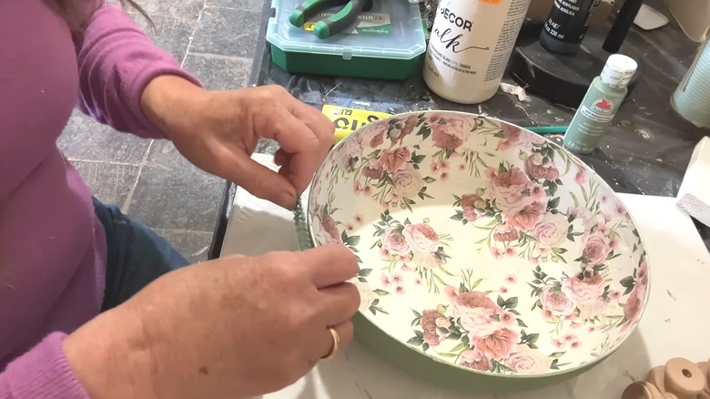 Woman adding lace trim to painted frying pan bowl with decoupage design