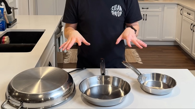 Man standing over three stainless steel frying pans in clean white kitchen