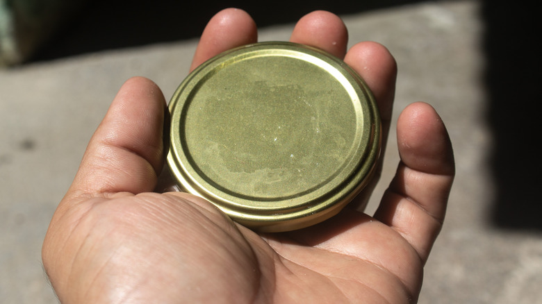 someone holds a golden jar lid in their hand
