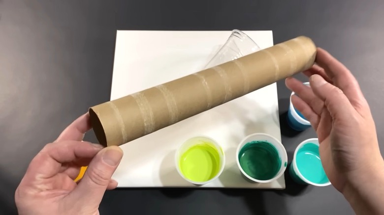 Person holding an empty paper towel roll with cups of paint for crafting