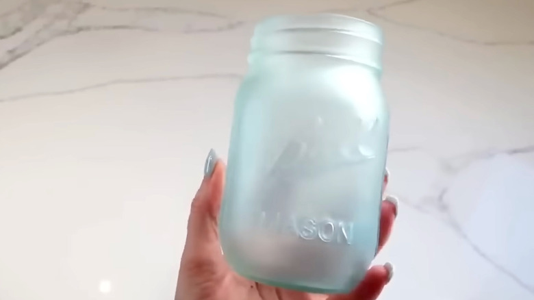 A hand holding a blue frosted mason jar