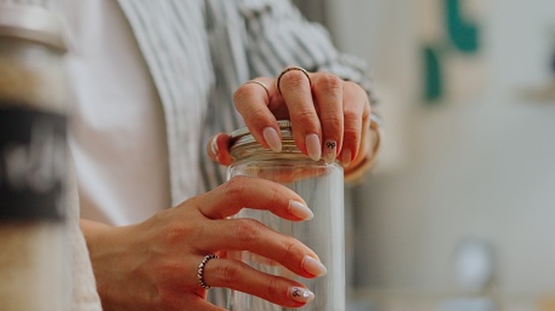 A woman unscrews the lid of a mason jar