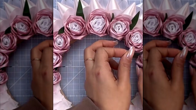 A hand attaches ribbon roses to a wreath base