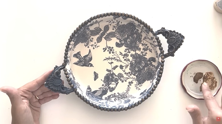 Old cooking pan upcycled into decorative dish with handles and bird and floral pattern on white table