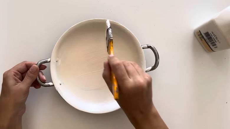 Young woman crafting with small pan, rope, and various common household tools on white surface