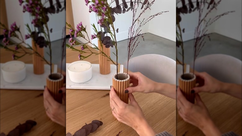 Hand holds empty paper towel roll turned into a vase with flowers in it