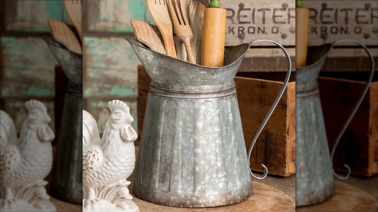metal pitcher with wooden utensils stored in it and chicken figurine beside it