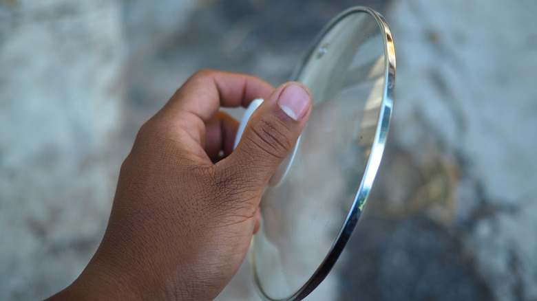 A hand holds a glass pot lid