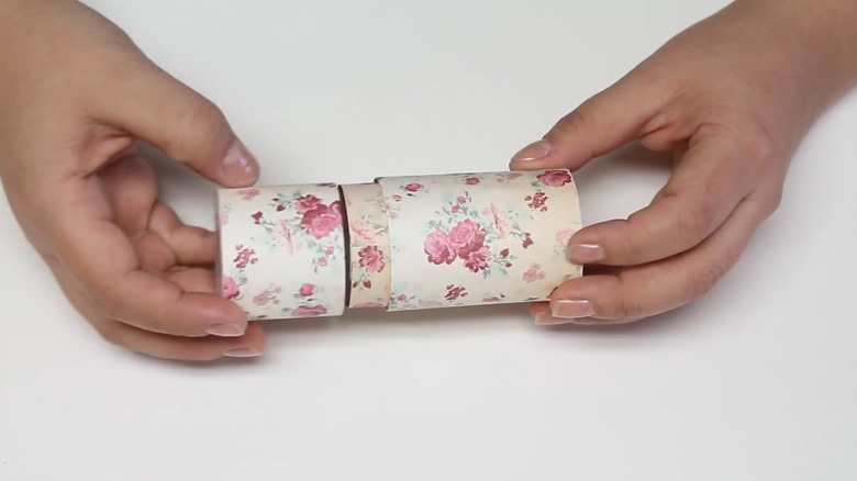 Person putting the lid on a round storage container made from toilet paper tubes covered in floral designs