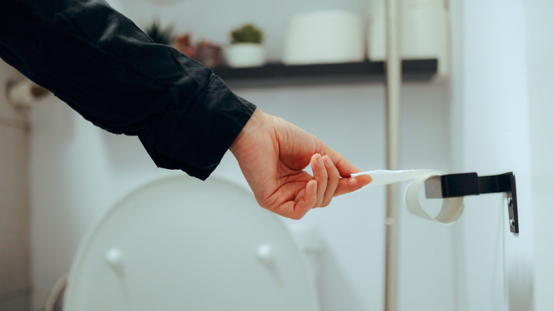 Hand reaching to pull the last of the toilet paper off of an empty roll