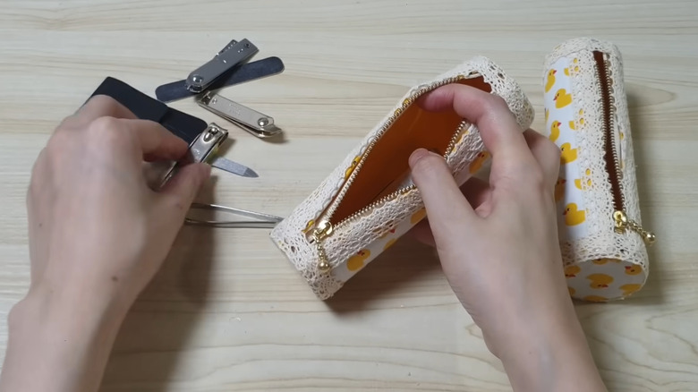 Person picking up nail clippers to put in a zippered container made from a toilet paper tube