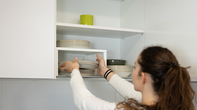 Woman carefully putting away plates in white kitchen cabinet