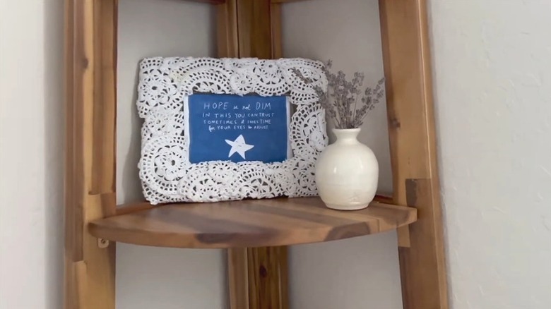 A DIY white doily picture frame with a blue text photo on a wooden shelf