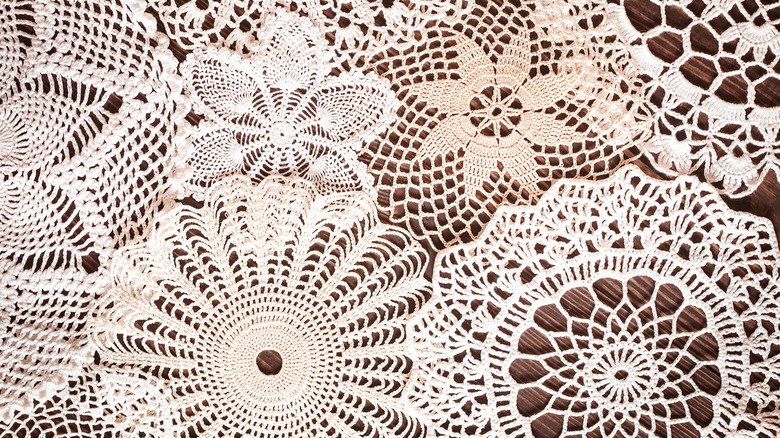 A variety of cloth doilies stacked one on top of the other on a wooden surface