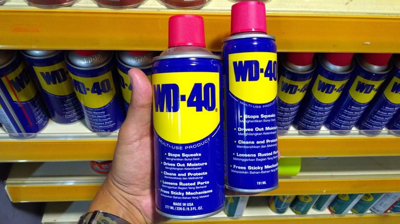 Person holding cans of WD-40 in front of a store shelf.