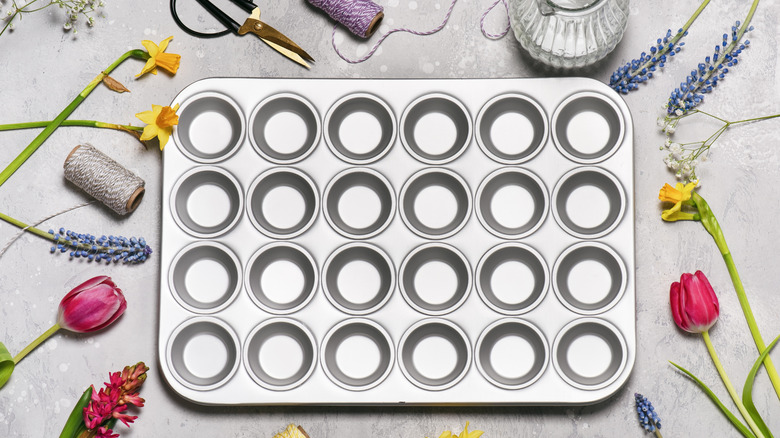 A muffin tin surrounded with flowers and craft supplies