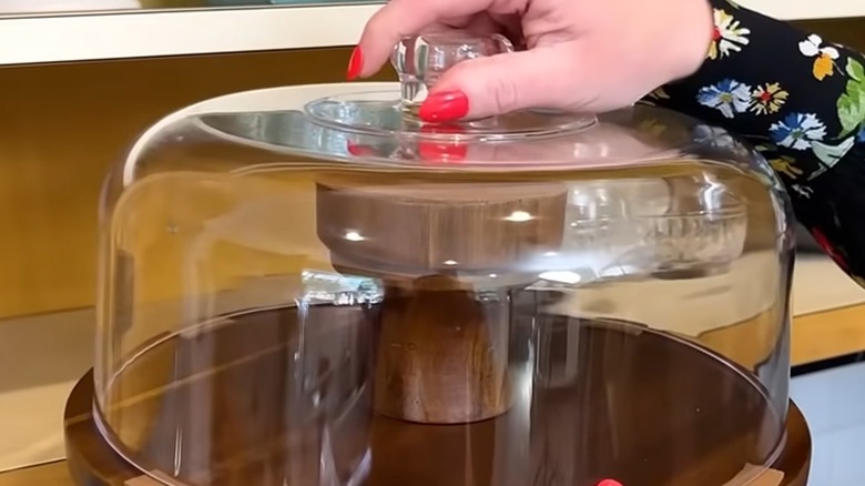 A woman with painted red nails holds the lid of a cake stand