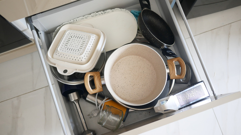 cabinet drawer with mess of pans, dishes, and other cooking equipment