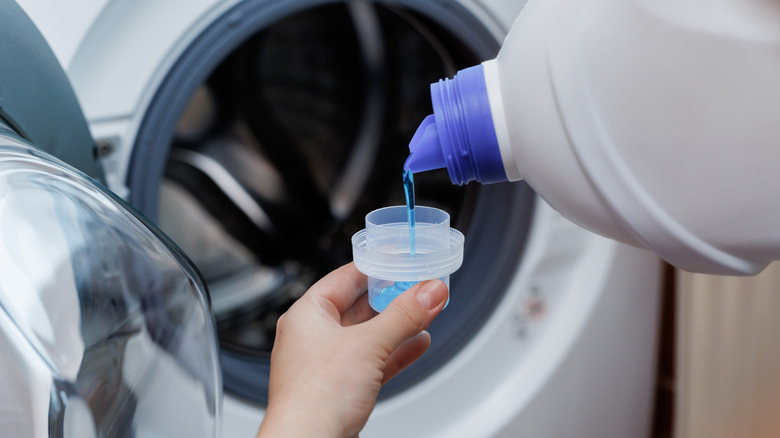 Person pouring detergent out of the bottle into the measuring cup lid